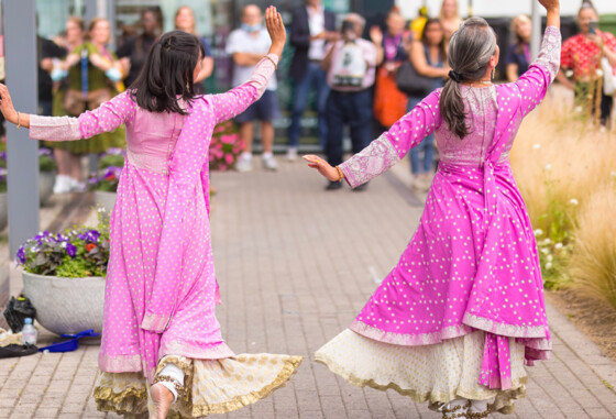 Two dancers wearing saris are performingoutside while a crowd looks on